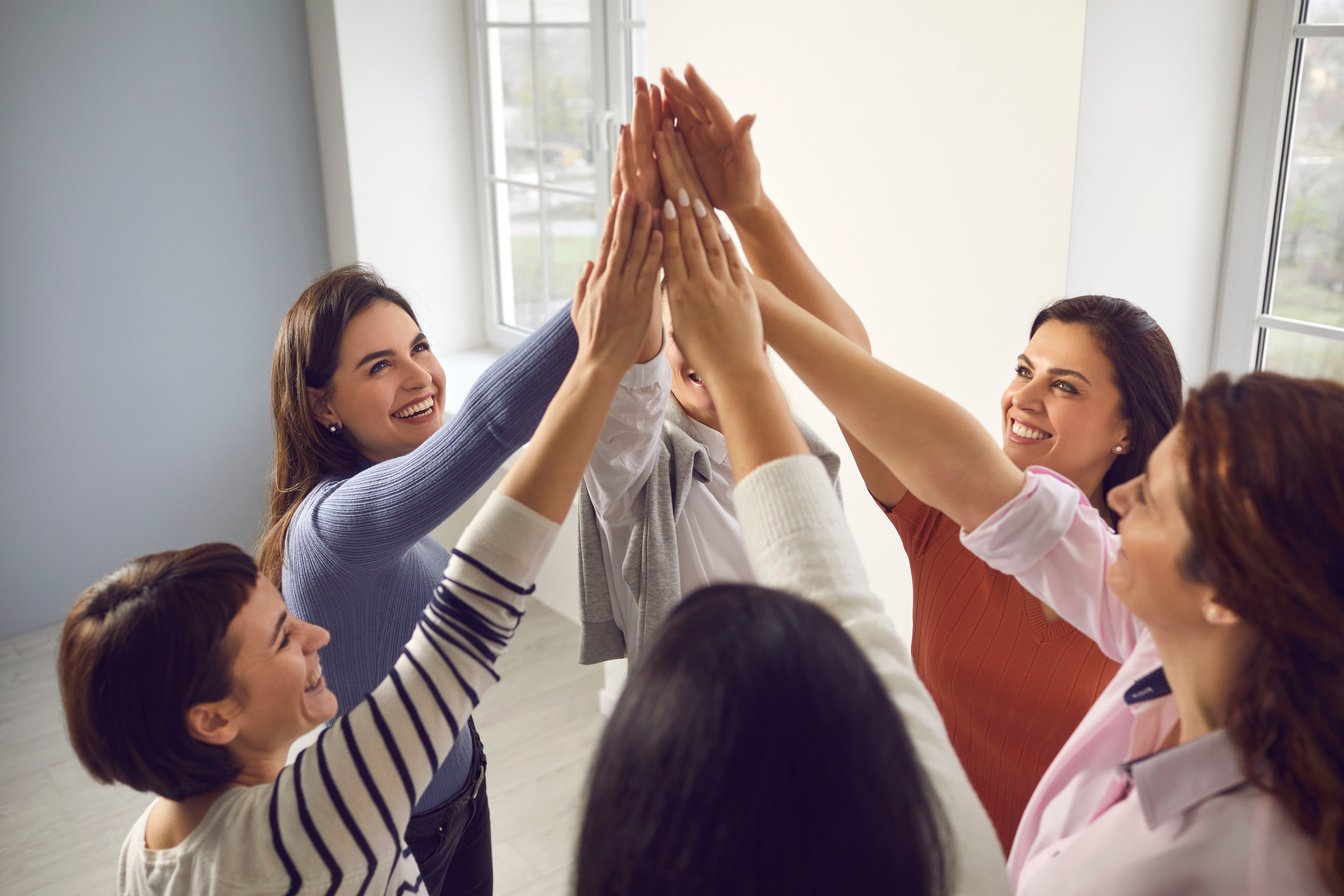 a team of women in business in an office with their hands in the air representing teamwork and employee engagement. 